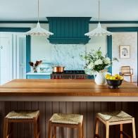 an island in the middle of a kitchen with three stools and a bowl of fruit on it