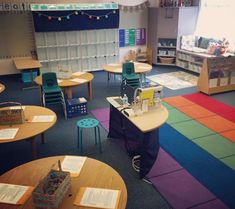 a classroom with tables, chairs and bookshelves filled with papers on the floor