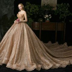 a woman in a gold wedding dress standing next to a table with flowers on it