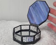 a hand is holding an empty ring box on a lace tablecloth with white and blue designs