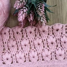 a pink crocheted blanket next to a flower on a table with yarn and scissors