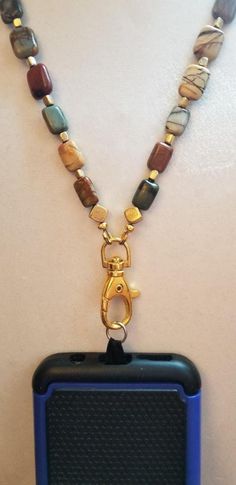 Very unique, one of a kind semi-precious stone cell phone lanyard.  Jasper stones are beautifully variegated in colors perfect for the fall.  Will go beautifully with fall and winter outfits of browns, burgundy and tans.  Combined with the gold toned beads and gold lobster claw clasp, the effect is very rich and stunning. Turn this piece around and it can be worn as a lovely necklace! This piece comes with tab to be inserted where the phone charger is inserted into the phone.   Fits both iPhones and Samsung. The length of this piece is 19 inches. Jasper Stone, Lovely Necklace, Badge Holders Lanyard, Lanyard, Cell Phone, Semiprecious Stones, Semi Precious, Halloween Shopping, Gold Tones