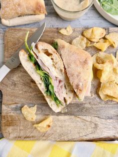 a cut in half sandwich sitting on top of a wooden cutting board next to chips