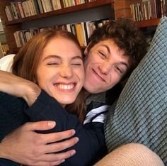 two people hugging each other on a couch in front of a book shelf with books