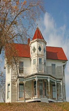 an old white house with a red roof sits on a hill in front of a tree