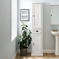 a bathroom with a sink, toilet and tall cabinet in it's corner next to a plant