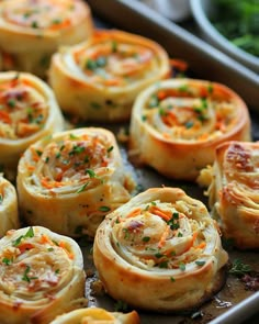 there are many small rolls on the baking pans with carrots and parsley