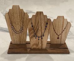 four necklaces are on display in a wooden stand with marble counter top behind them