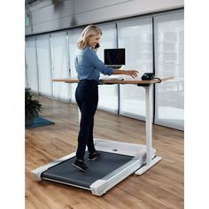 a woman on a treadmill talking on her phone and holding a laptop in one hand