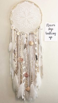 there is a white wall hanging with beads and feathers on it, next to a sign that says never stop looking up