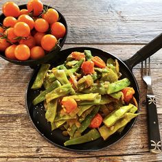 a black plate topped with asparagus and tomatoes next to a bowl of oranges