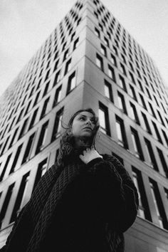 a woman standing in front of a tall building talking on her cell phone while looking up at the sky