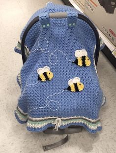 a blue crocheted baby seat cover with two bees on it in a store