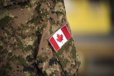 a canadian flag patch on the chest of a soldier's camo uniform,