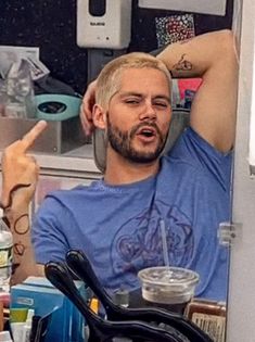 a man with his hand on his head sitting in front of a refrigerator and pointing to the side