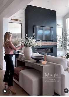 a woman standing next to a couch in a living room with a tv on the wall