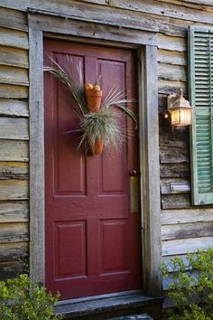 a red front door with green shutters and potted plants on the side of it