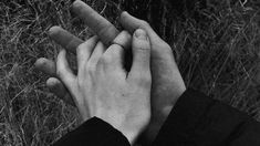 two hands reaching out towards each other in front of some tall grass and weeds,