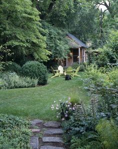 a garden with stepping stones leading up to a small shed in the background, surrounded by greenery and trees