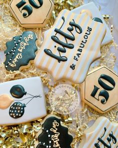 decorated cookies with black and white frosting are on a gold foiled tablecloth