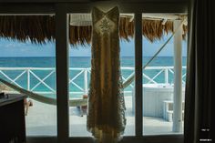 a wedding dress hanging in front of a window with the ocean and beach behind it