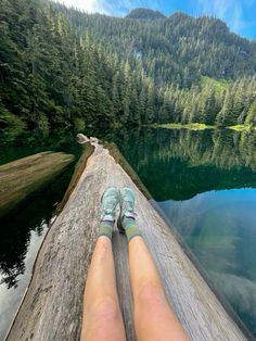 someone's feet resting on the edge of a log over water