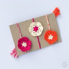 three crocheted ornaments on top of a piece of brown paper with red and white tassels