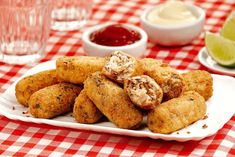 some fried food on a white plate with dipping sauce and limes in the background