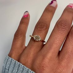 a woman's hand with a diamond ring on her finger and pink nail polish