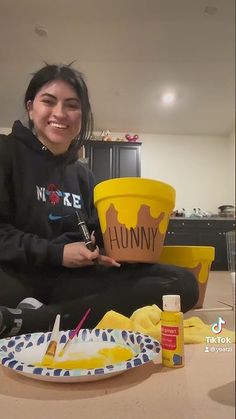 a woman sitting on the floor holding a yellow bucket and painting it with her hands