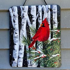 a red cardinal sitting on top of a pine tree in front of snow covered trees