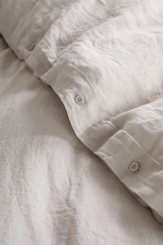 an unmade bed with white linens and buttons on the collared shirting