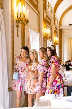 four beautiful young women standing next to each other in front of a mirror and chandelier