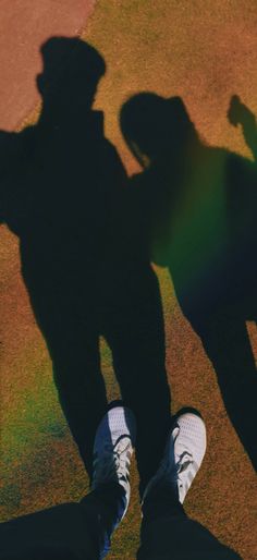 two people standing next to each other on top of a grass covered field with their shadows