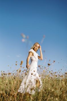 a woman in a white dress is walking through tall grass with her hand on her head