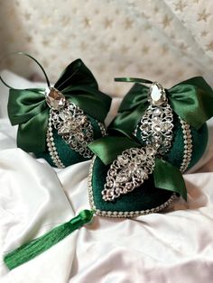 two green heart shaped brooches sitting on top of a white cloth covered bed