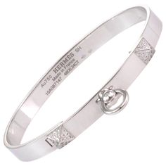 This stunning Collier de Chein collection is by Hermes, it features an authentic bangle crafted from 18k white gold with a high polished finish featuring a 6mm wide band. The front of the bangle has two small pyramid like design set with diamond and the center has a door knocker ring dangling below. It is signed by the designer with the serial number, gold content and diamond weight. Brand: Hermes Hallmark: Au750 Hermes SH Made in France 16A087147 48D0.24ct Diamond: 0.24ct (48 diamonds) Material Luxury Hallmarked White Gold Cuff Bracelet, Luxury Polished Bangle, Luxury Round Bangle With Polished Finish, Luxury Polished Round Bangle, Luxury Diamond Bangle With Polished Finish, Luxury Polished Diamond Bangle Bracelet, Luxury Engraved Diamond Bracelet, Designer Polished Bangle Jewelry, Designer Polished White Gold Jewelry