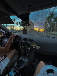 two people are driving down the street in their car at sunset or dawn with palm trees