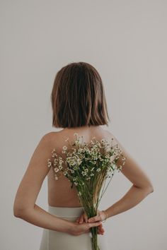 the back of a woman's body with flowers in her hand and behind her is a bouquet of baby's breath