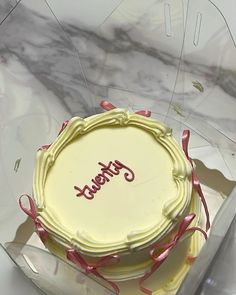 a white cake in a clear box with pink ribbon around the edges that says happy