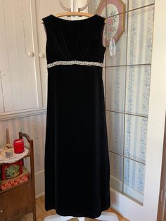 "This is one of the most elegant dresses I have ever seen! From Leda Design, it's made of heavier weight black velvet and fully lined with black silky lining. It has a gathered empire waist adorned with pale metallic gold trim that comes to a \"v\" in the back. The dress fastens with a long back zipper. Marked size 40. The measurements, taken with the dress lying flat, are: shoulder to shoulder, 15 inches; armpit to armpit, 17 inches; waist, 15 inches; length, 52 inches; bottom edge, 29 inches. The trim around the waist shows some wear, but the dress is in very good condition." Black Velvet Gala Dress, Sleeveless Velvet Dress For Wedding, Black Velvet Evening Dress For Holidays, Sleeveless Velvet Evening Dress For Gala, Sleeveless Velvet Wedding Dress, Black Velvet Holiday Evening Dress, Holiday Black Velvet Dress, Black Velvet Maxi Dress For Formal Occasions, Vintage Black Gown