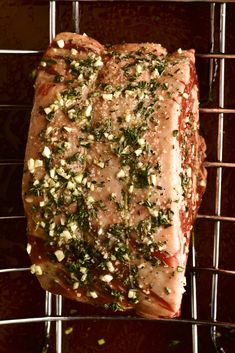 a piece of meat sitting on top of a metal rack covered in seasoning and herbs