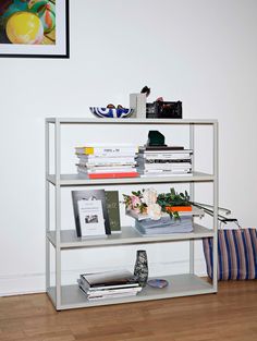 a book shelf with books and magazines on it in front of a wall mounted painting