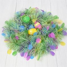 an arrangement of colorful easter eggs in a basket on a white table with pine branches