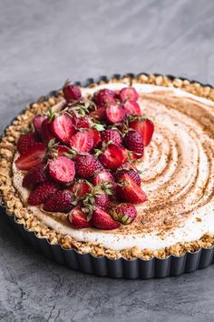 a pie topped with strawberries on top of a black pan covered in frosting