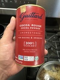 a person is holding a can of cocoa powder in front of an open stove top