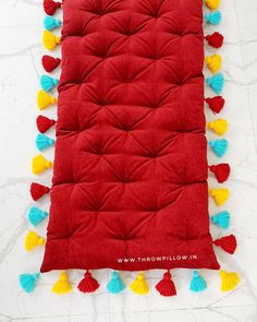 a red pillow with tassels on it sitting on top of a white floor