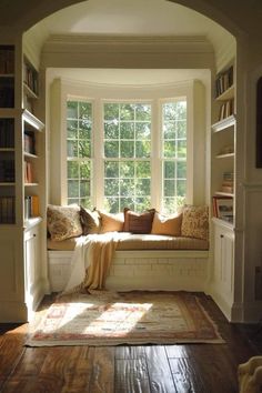 a window seat with pillows on it in front of a book shelf and bookshelves