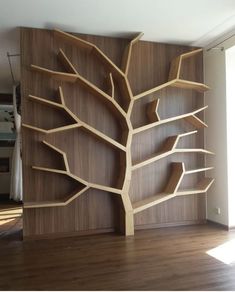 a wooden bookcase with shelves and a tree on the wall in front of it