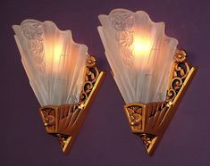 two wall sconces with glass shades on them against a purple wall in a room